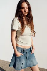 Falda mini de jean con diseño de tablas, tiro medio, bolsillos delanteros y cierre frontal con botones.