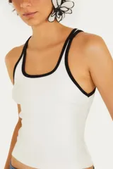Top tipo musculosa de tejido acanalado blanco, con escote cuadrado y ribetes negros en el borde del escote y las sisas. Presenta doble tirante fino negro.