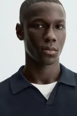 Jersey de punto color verde oliva, de calce relajado (relaxed fit), con cuello solapa y abertura frontal en forma de V. Es de manga corta y presenta acabados en rib en puños y ruedo.