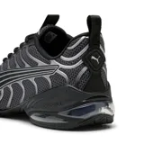 Championes Puma modelo Voltra, color negro con detalles plateados. Presentan un diseño técnico con malla transpirable, refuerzos sintéticos y tecnología X-CELL en la suela para mayor amortiguación.