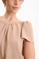 Blusa de manga corta con pliegues en escote redondo, confeccionada en tela crepé de color beige.