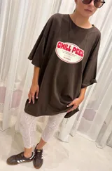 Remera oversize color crema con estampa central circular en color rojo que incluye el texto 'Chill Peel'. Presenta cuello redondo y mangas cortas con un ajuste holgado.