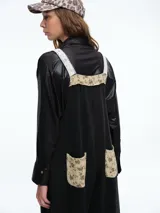 Mono largo de color negro con corte holgado y perneras anchas. Presenta detalles de encaje blanco y tela estampada floral en los tirantes, el bolsillo frontal, la parte inferior de las piernas y el ruedo.