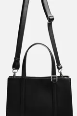 Bolso tipo shopper color negro, con compartimento principal con cierre mediante imán, bolsillo interior con cierre, detalle de arnés en la parte delantera, dos asas de mano y asa de hombro ajustable y extraíble.