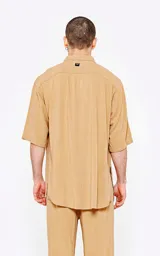 Camisa de corte oversize, color beige, con cuello clásico, cierre frontal de botones y mangas cortas. Confeccionada en tejido de lino.