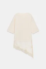 Remera color crema de algodón, corte recto, cuello redondo y mangas cortas. Presenta un panel asimétrico de encaje en el ruedo.