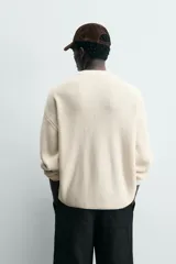 Cárdigan de punto color crema, con cuello pico, manga larga y cierre frontal de botones marrones. Presenta un calce relajado y acabados en rib.