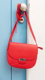 Bandolera de cuero sintético en color rosado, con diseño de solapa redondeada y cierre metálico frontal. Cuenta con correa ajustable para llevar al hombro o cruzada.