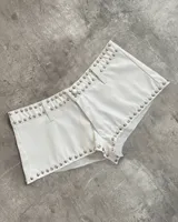 Short de tiro medio confeccionado en cuero sintético color blanco, con diseño de tachas metálicas plateadas en todo el contorno de la cintura y los bordes inferiores.