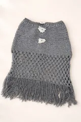 Pollera mini tejida en crochet color gris, con diseño de punto calado en la parte inferior y terminación con flecos. Presenta botones decorativos de nácar en la parte superior.
