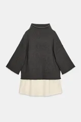 Jersey de punto color gris oscuro, con cuello alto y mangas anchas a tres cuartos. Presenta un bajo superpuesto de tejido satinado color crema o blanco roto.