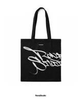 Tote bag negra de lona premium con diseño de graffiti en color blanco estampado en el frente. Cuenta con dos asas largas para llevar al hombro.
