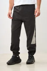 Pantalón de jogging gris oscuro con banda lateral gris claro, cintura elástica con cordón ajustable, bolsillos laterales con cierre y puños elásticos.