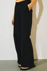 Pantalón de tiro medio color negro con trabillas en la cintura, bolsillos laterales ocultos y pierna recta. Cierre frontal con cremallera, botón y ganchos metálicos.