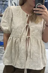 Blusa beige de lino bordado, calce holgado, escote en V con doble lazo ajustable y mangas 3/4 con volumen.