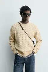 Sweater de punto con diseño de trenzas, color beige, cuello redondo y manga larga con terminaciones en rib.