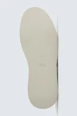 Zapatilla de cordones color blanco hueso, con parte superior lisa y suela de plataforma gruesa. Presenta un detalle de pieza negra en el talón.