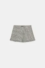 Falda corta de tiro medio confeccionada en tejido de tweed con textura, en tonos blanco y negro. Presenta pinzas en el delantero, bajo con terminación desflecada y cierre lateral con cremallera oculta.