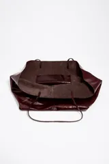 Bolso shopper grande Bimba Y Lola confeccionado en cuero vacuno con acabado brillante en color bordó. Cuenta con estructura blanda, doble asa fina de hombro y detalle de logo metálico en la parte inferior.