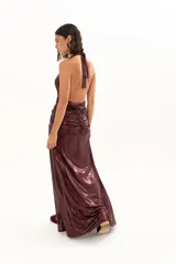 Vestido largo de fiesta en tejido brillante color bordó, con escote halter profundo, detalle de frunces en la cintura y tajo lateral en la falda.