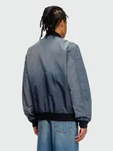 Campera bomber Diesel modelo J-Kepes, color gris azulado con efecto desgastado o tie-dye sutil. Presenta cuello, puños y cintura de punto elástico en color negro. Lleva un parche grande con el logo 'D' de Diesel en el pecho izquierdo.