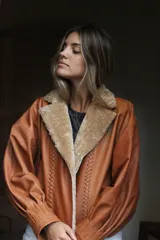 Campera oversize de cuero tostado con solapas y forro interno de corderito sintético azul marino, mangas anchas y detalles de costuras trenzadas.
