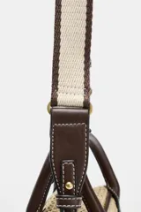 Bolso pequeño tipo bowling de rafia tejida en color natural, con ribetes, asas de mano y detalles en cuero marrón oscuro. Incluye un charm colgante con candado dorado y una correa ajustable extraíble para llevar al hombro o cruzado.