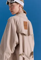 Trench midi color camel, confeccionado en mezcla de algodón y nylon. Presenta cuello clásico, cierre frontal con botones, tajos laterales y bolsillos internos. Es una prenda repelente al agua con diseño versátil y funcional.
