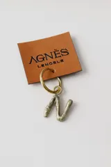 Caravana individual de la marca Agnès Lenoble confeccionada en bronce. Presenta un diseño de aro pequeño con un dije colgante en forma de letra 'N' con textura irregular y acabado rústico.