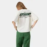Remera oversized color blanco crema, con cuello redondo y mangas cortas. Presenta un estampado en la espalda con el logo de "Eme Studios" en verde y texto "Building a community through gratitude".