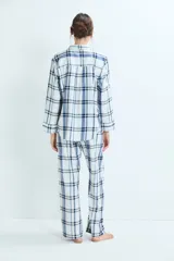 Pijama de dos piezas con estampado de cuadros en tonos azules y blancos. La parte superior es una camisa de manga larga con cuello camisero y cierre frontal de botones. La parte inferior es un pantalón de corte recto con cintura elástica.