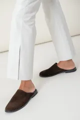 Zuecos de gamuza color marrón chocolate con suela plana y detalle de tachas pequeñas alrededor de la suela.