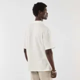 Remera de punto color blanco, de manga corta, con cuello solapa y diseño holgado.