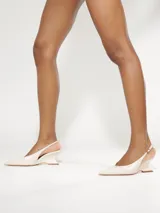 Zapato slingback Schutz de color blanco, con punta fina, diseño abierto en los laterales y taco geométrico bajo. Cuenta con una tira ajustable en el talón con hebilla metálica.