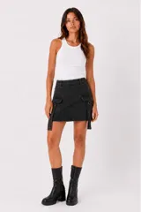 Falda mini de jean color negro, con diseño cargo que incluye bolsillos laterales con solapa y tiras decorativas colgantes.