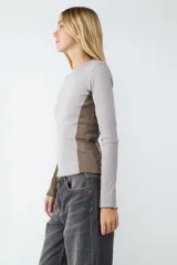 Remera de manga larga en tejido jersey, con diseño de bloques de color en tonos gris y marrón. Presenta un calce ajustado, cuello redondo y terminaciones con borde ondulado.