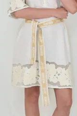 Vestido corto de lino blanco con cuello clásico, mangas cortas y detalles bordados florales tono sobre tono con inserciones translúcidas. Incluye un cinturón de tela ajustable con estampado.