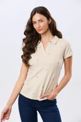 Remera polo de algodón color beige con mangas cortas, escote en V y cuello camisero. Presenta delicados mini bordados florales distribuidos en toda la prenda.