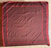 Pañuelo de seda rojo con estampado geométrico negro en el centro y cenefa de diseño greca en los bordes.