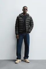 Campera puffer acolchada de corte regular fit en color negro, confeccionada en tejido técnico repelente al agua. Presenta cuello subido con capucha, cierre frontal de cremallera, mangas largas con puños elásticos y bolsillos laterales de vivo.