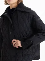 Campera matelaseada de corte recto y largo a la cadera, con cuello y puños de tejido acanalado. Presenta cierre frontal con broches grabados, bolsillos plaqué en el frente y cordón ajustable en el cuello.