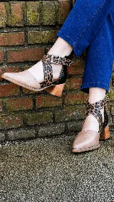 Zapatos de cuero color tostado con puntera fina y taco bloque de madera de 6 cm. Cuentan con tiras cruzadas con estampado animal print de leopardo en el empeine, talón negro y tira al tobillo con hebilla metálica ajustable.