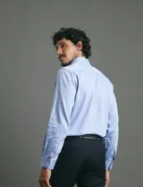 Camisa de vestir de manga larga en color azul claro, con cuello clásico, cierre frontal de botones y bolsillo en el pecho.