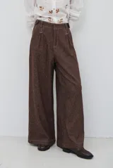 Pantalón de corte ancho y tiro alto, confeccionado en tejido con textura de espiga en tono marrón oscuro. Presenta pinzas en la parte frontal, cierre con botón y costuras a la vista en contraste.