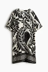 Vestido túnica de corte holgado con cuello mao y abertura en V. Presenta mangas cortas con hombros caídos, bajo recto con tajos laterales y un diseño estampado de hojas en contraste blanco y negro.