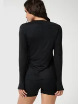 Polera de manga larga técnica, color negro, con cuello redondo y diseño ajustado. Presenta aberturas para los pulgares en los puños y un pequeño logo reflectante en el pecho.