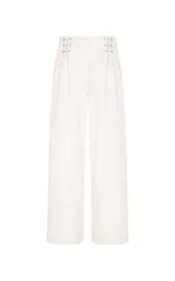 Pantalón sastrero de lino y algodón color beige, de tiro alto y corte ancho (wide leg). Presenta sutiles pliegues frontales, trabillas con apliques metálicos dorados en la cintura y bolsillos laterales.