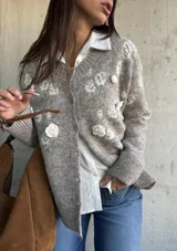 Cardigan de punto color beige con diseño de flores bordadas en relieve, cuello redondo, cierre frontal con botones y puños acanalados.