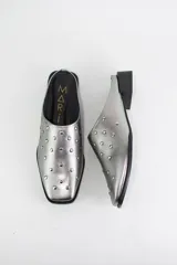 Zueco de cuero color plateado con punta almendrada y detalle de tachas metálicas distribuidas en toda la capellada. Cuenta con un taco cuadrado bajo de 3 cm.
