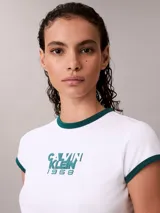 Remera Calvin Klein ajustada de color blanco, con cuello redondo y ribetes en las mangas de color verde oscuro. Presenta un estampado gráfico frontal con el texto "Calvin Klein 1968" en tono verde.